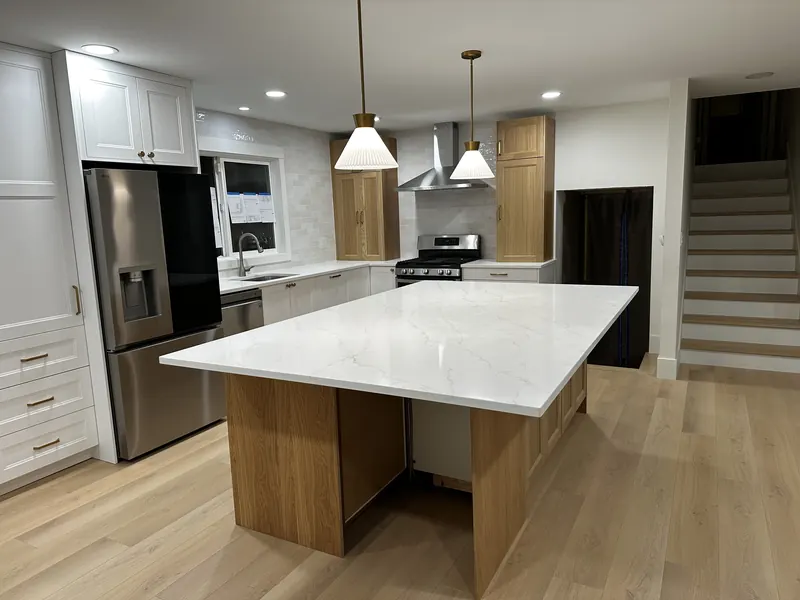 After: the new kitchen with a white quartz island on an oak base, pendant lights and light oak floors