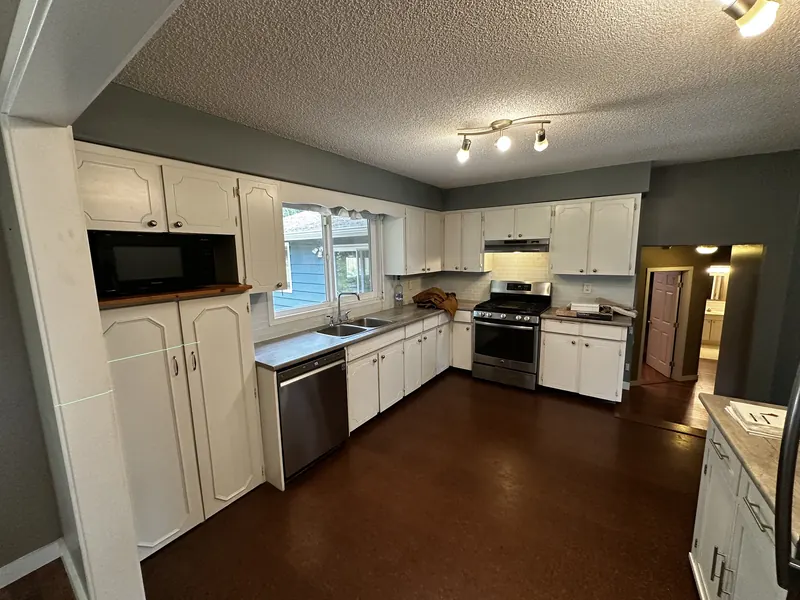 Before: the original kitchen with white cabinets, dark hardwood floors and a textured ceiling